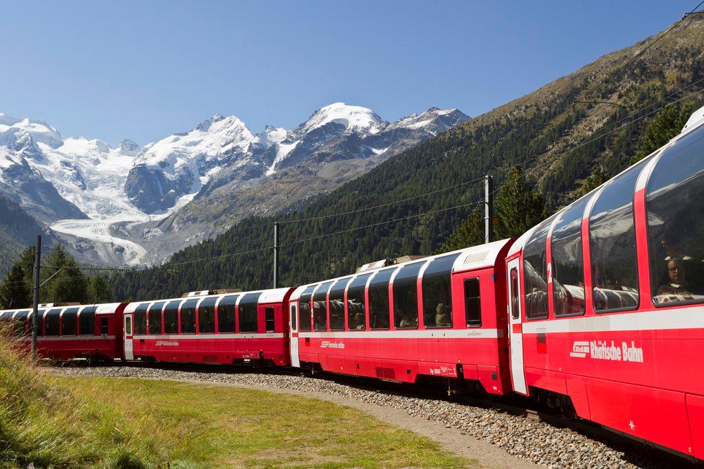 Convoglio ferroviario di carrozze panoramiche visto di profilo in paesaggio di alta montagna, cime innevate