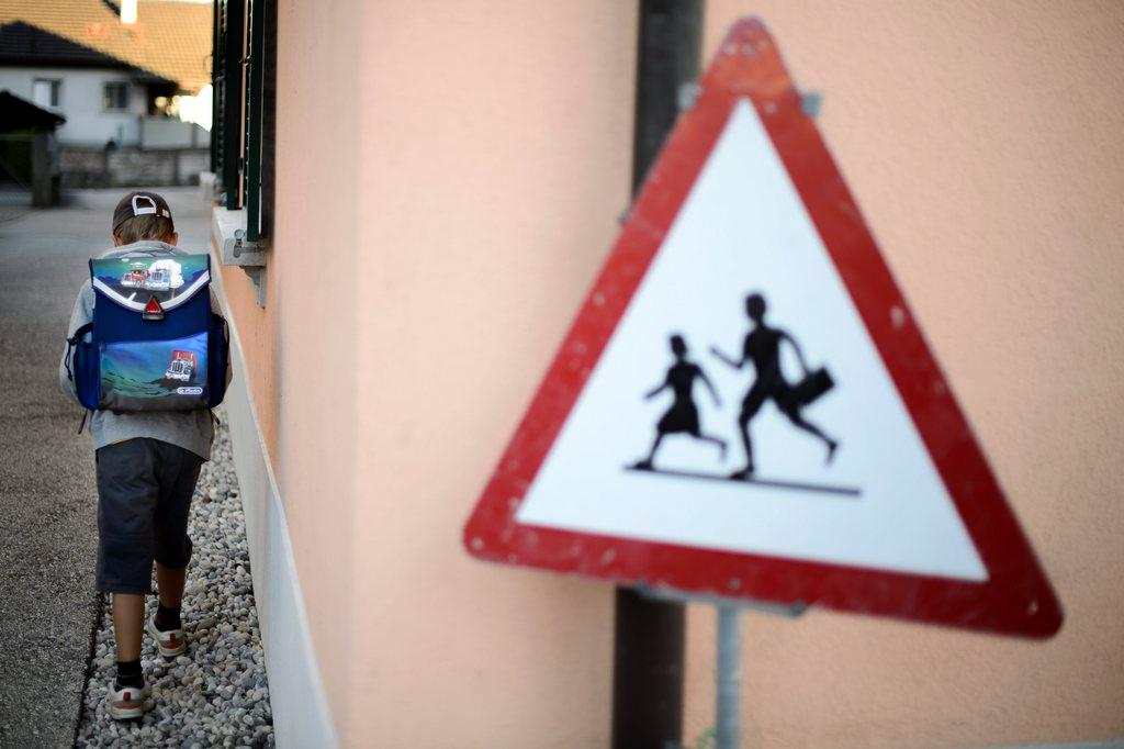 Un niño de espaldas con una mochila y una señal de tránsito que indica que hay una escuela