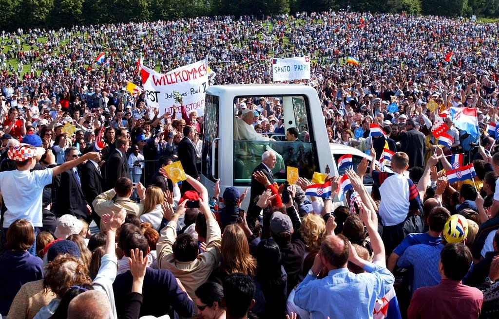 A crowd of people surround the pope who is sitting in the Popemobile.
