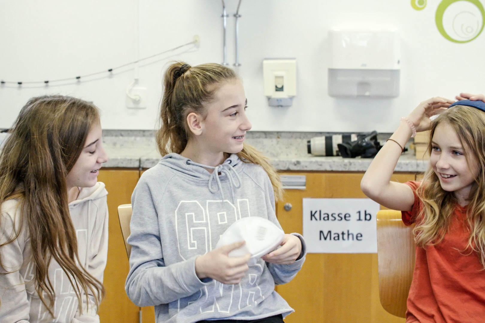 Drei Mädchen im Klassenzimmer probieren sich Kippas aufzusetzen.