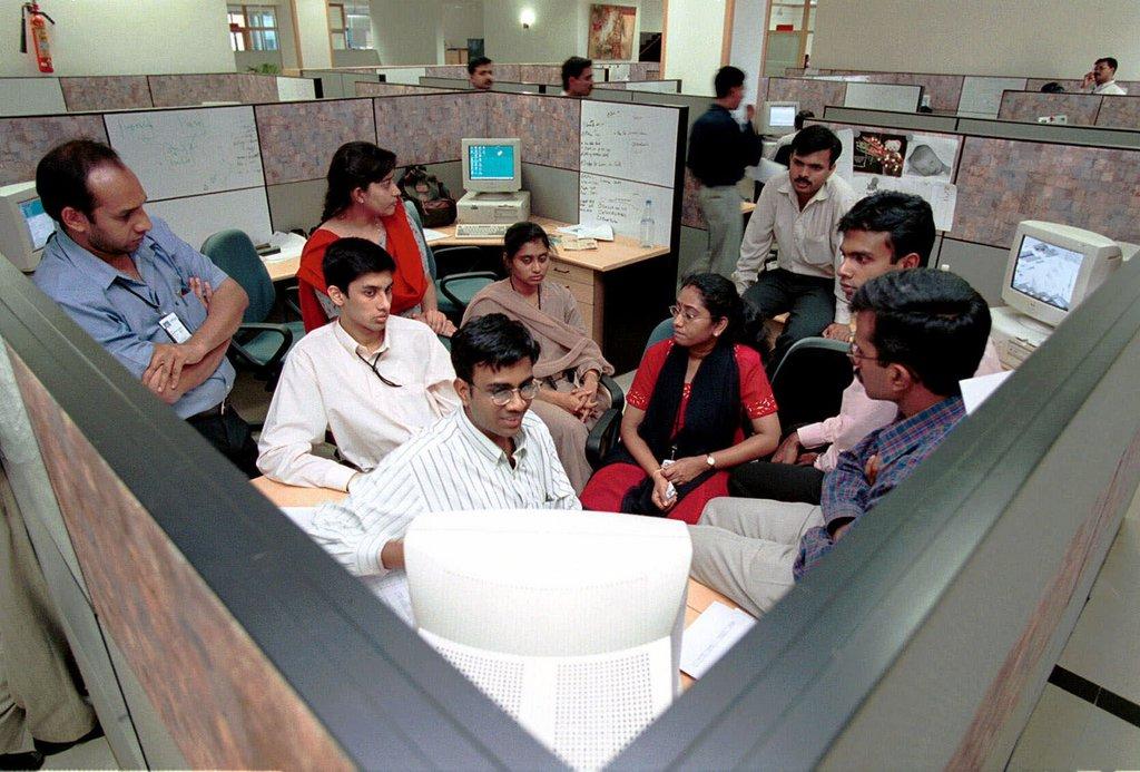 People gathered around a computer in an office cubicle.
