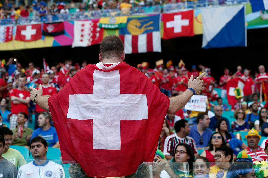 Un tifoso ricoperto da una bandiera svizzera, gira le spalle al campo e guarda verso il pubblico.