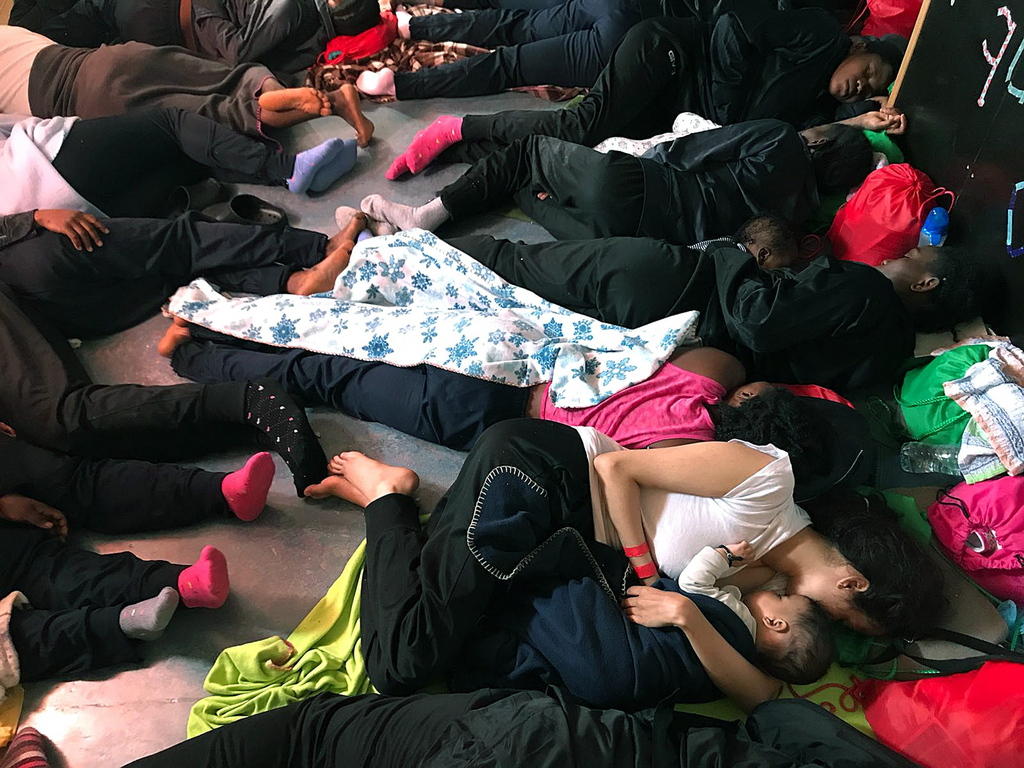 Adulti e bambini riposano sdraiati per terra, apparentemente sul ponte di una nave