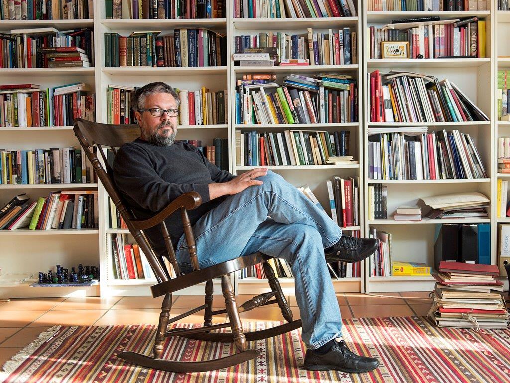 Un uomo è seduto su una sedia a dondolo davanti a uno scaffale pieno di libri