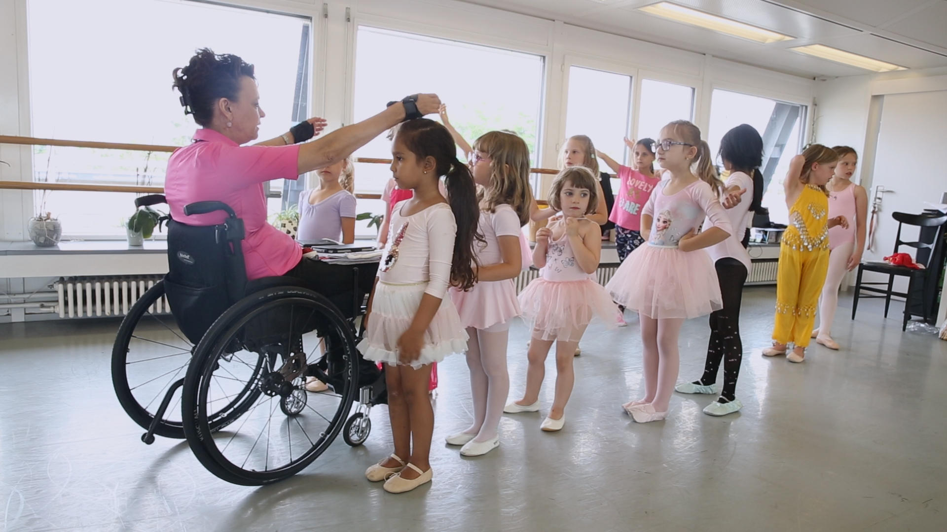 Teacher in wheelchair holds her hands above a child dancer