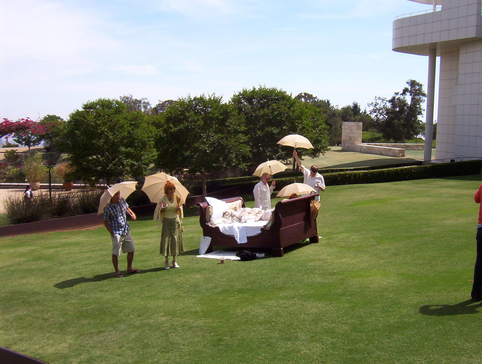People carrying umbrellas walk around bed on lawn