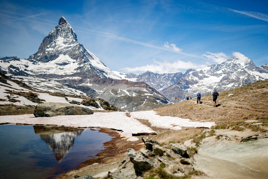 persone camminano su un sentiero in montagna sullo sfondo di una vetta innevata