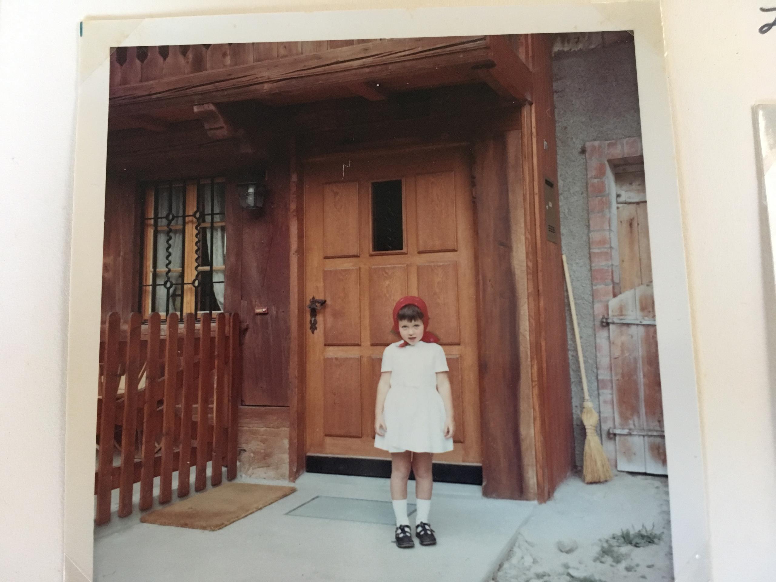 Old photo of Claudia Bucher as a child standing in front of door of farmhouse