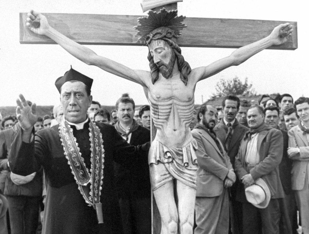 Una scena di un film con Don Camillo in processione con un crocifisso.