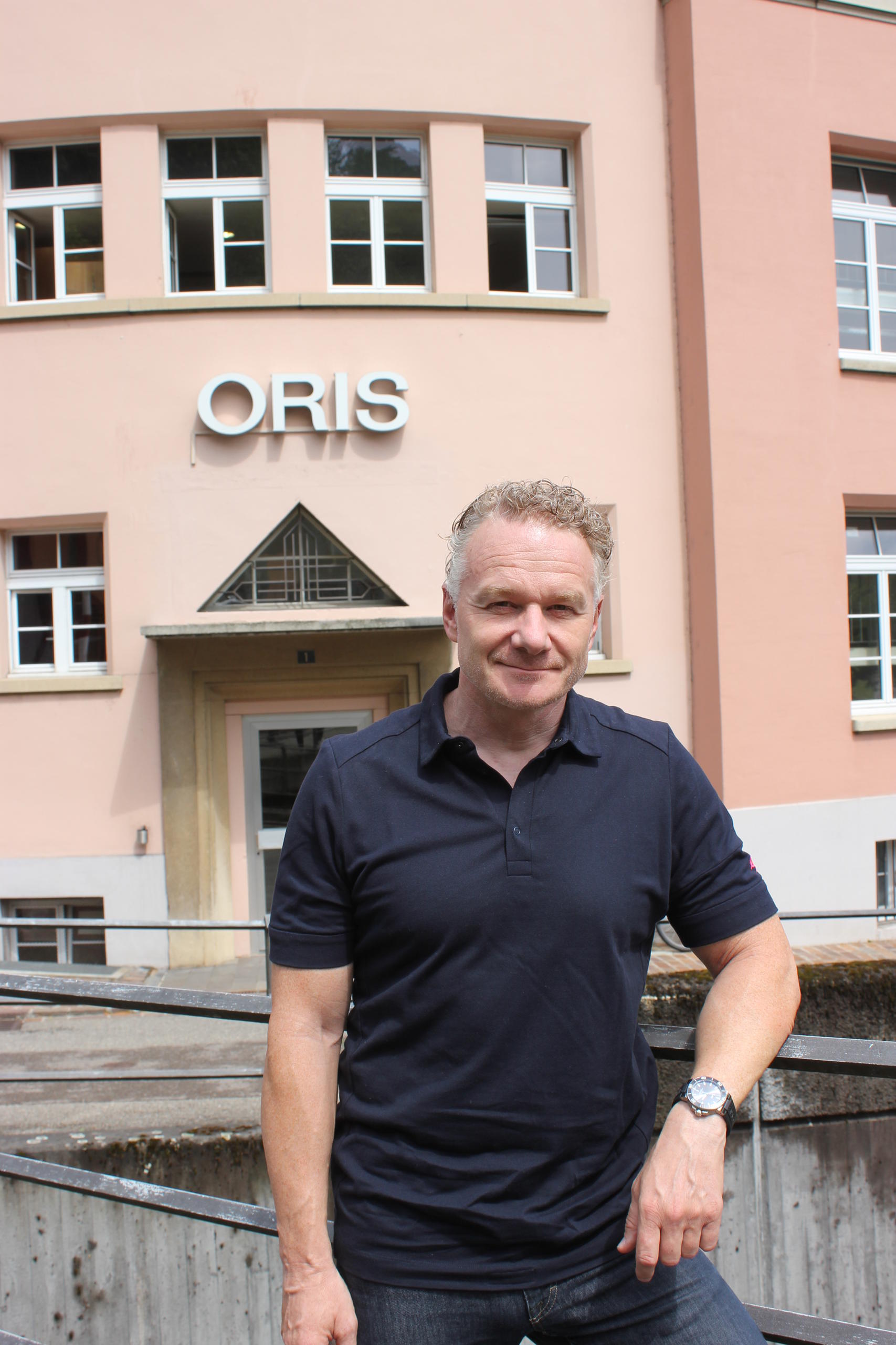 Mann in schwarzem Poloshirt vor einem Firmeneingang mit Beschriftung ORIS