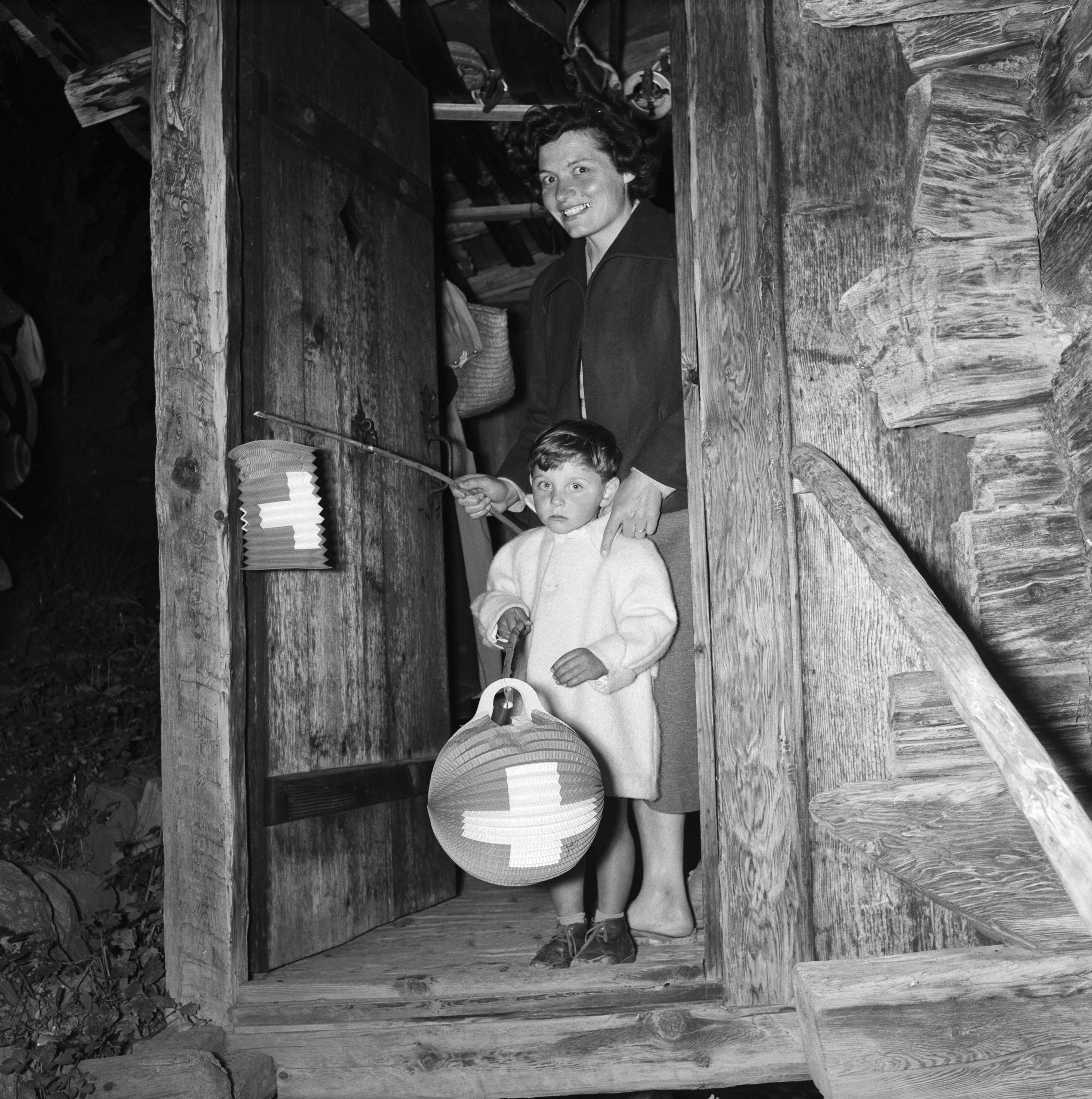 Mutter und Kind mit Lampions stehen in einem Türrahmen eines Holzhauses