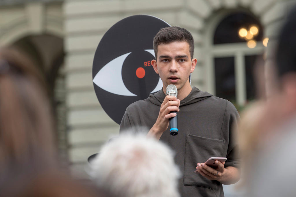 Rougy with mic and mobile phone addressing people outside parliament