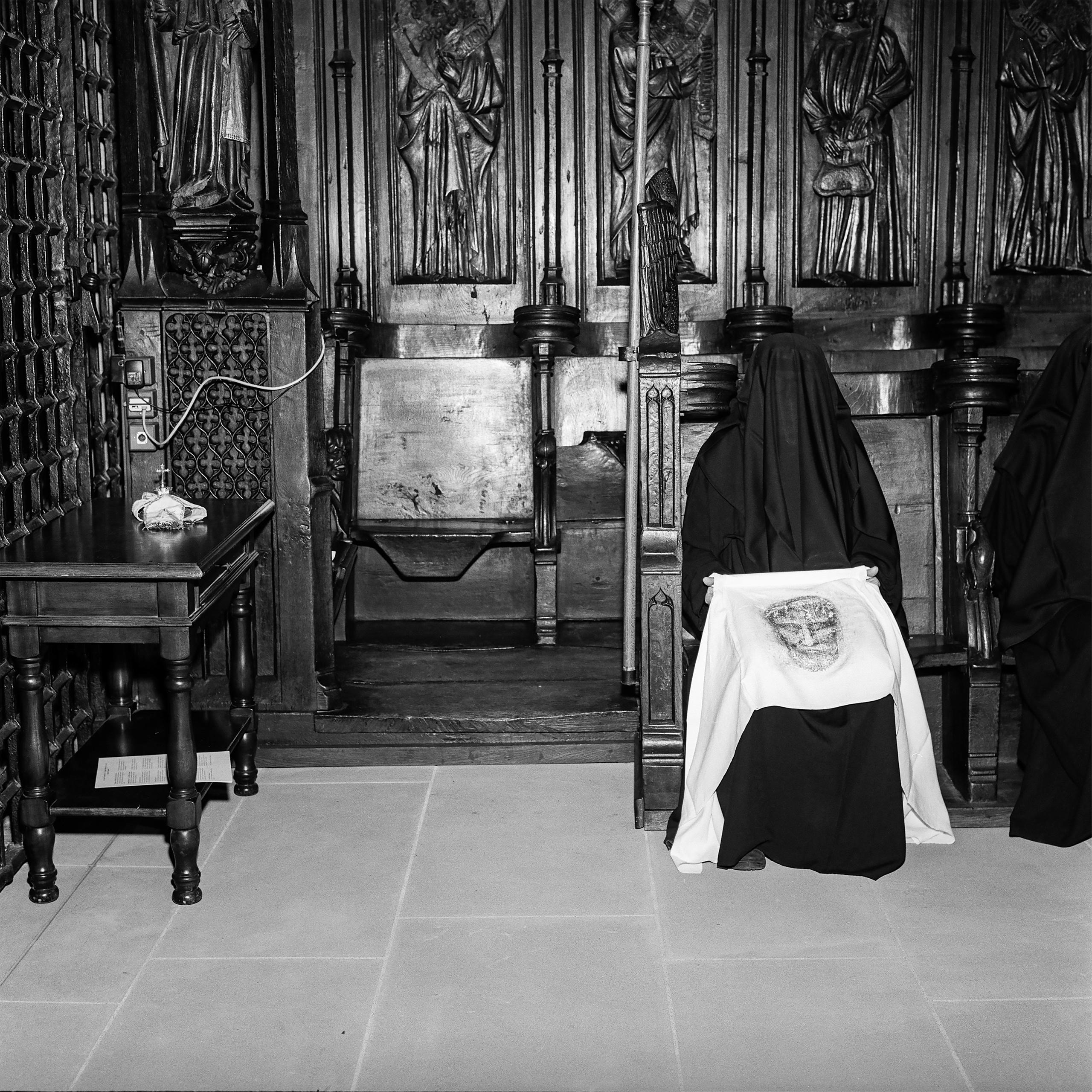 Frau in Schwarz sitzt auf Holzbank in der Kirche und hält ein Tuch mit Christuskopf