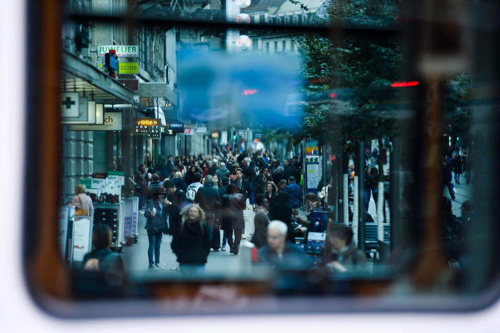 Persone che camminano in una via di città viste specchiate attraverso il finestrino di un tram