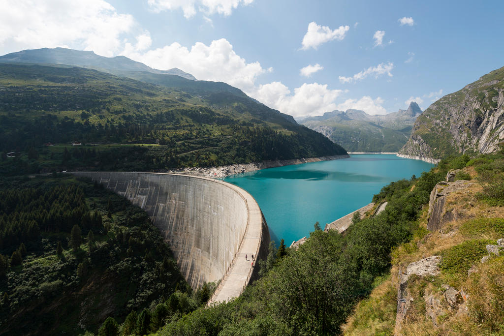 Una diga e relativo lago artificiale viste in una giornata di sole da una delle montagne circostanti.