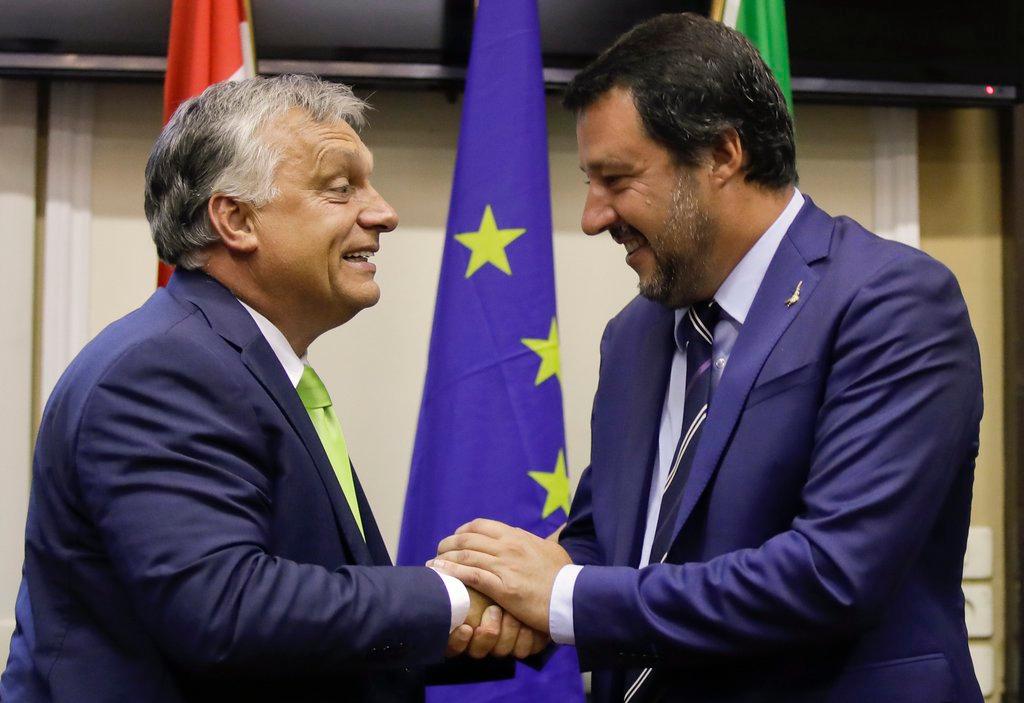 Orban e Salvini, di profilo e a mezzobusto, si stringono la mano. Sul fondo le bandiere ungherese, europea, italiana