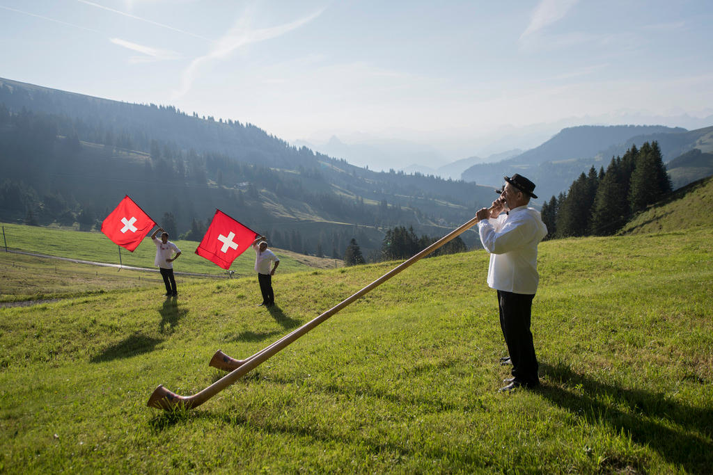 Due suonatori di corno alpino su un prato. Sbandieratori con bandiera svizzera sullo sfondo