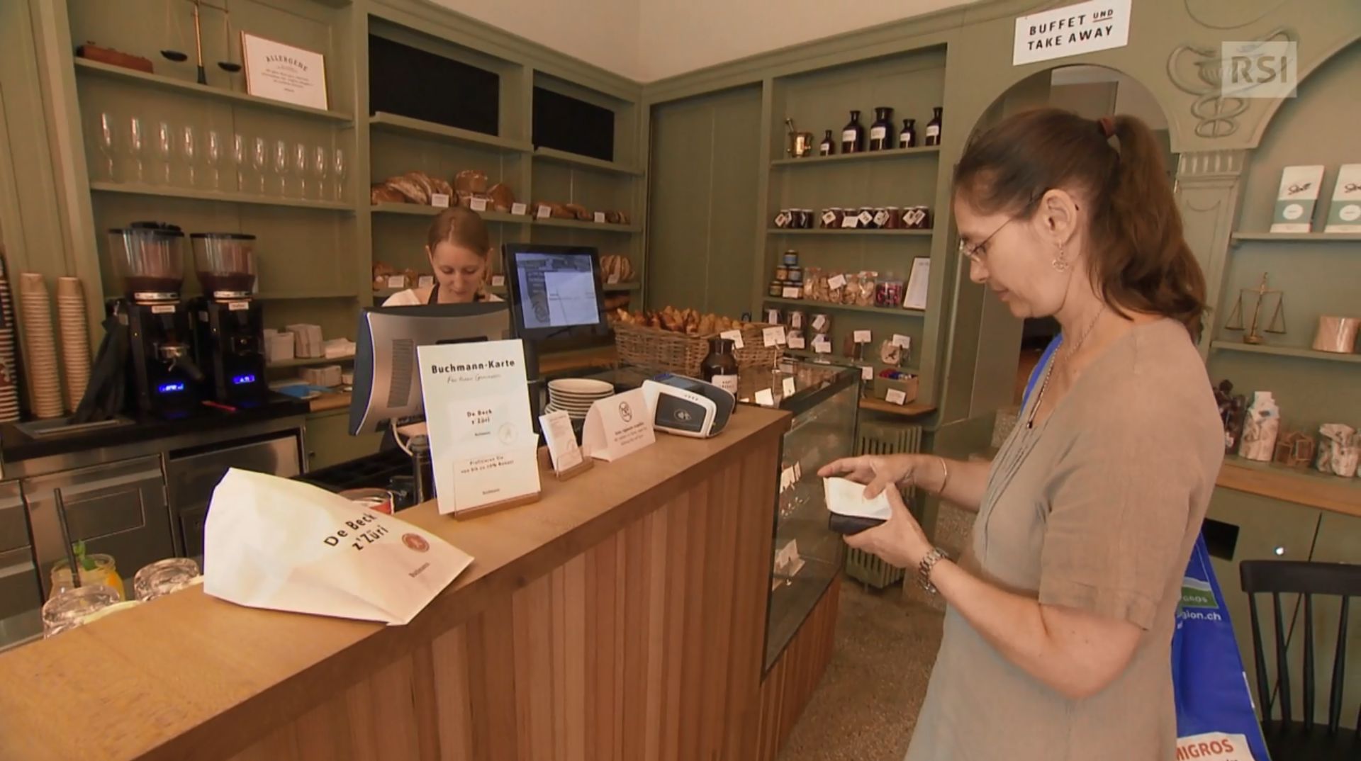 Una commessa di panetteria guarda lo schermo del computer mentre una cliente rimette in borsa il portafogli