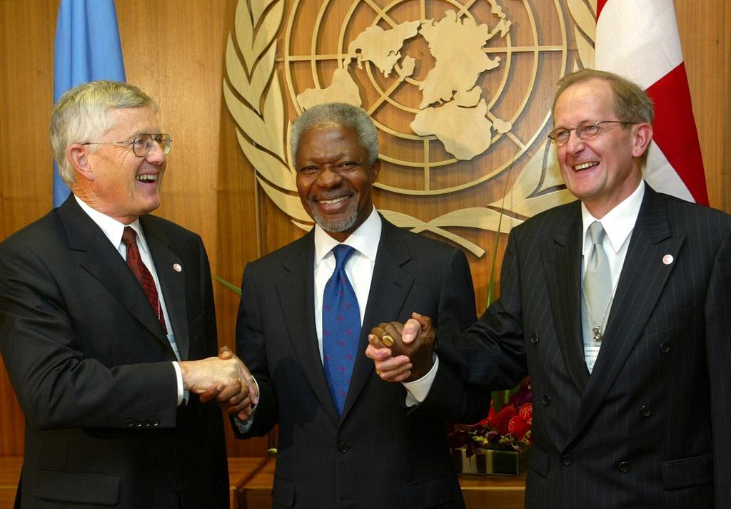 ثلاثة رجال أمام شعار الأمم المتحدة وعلم سويسرا