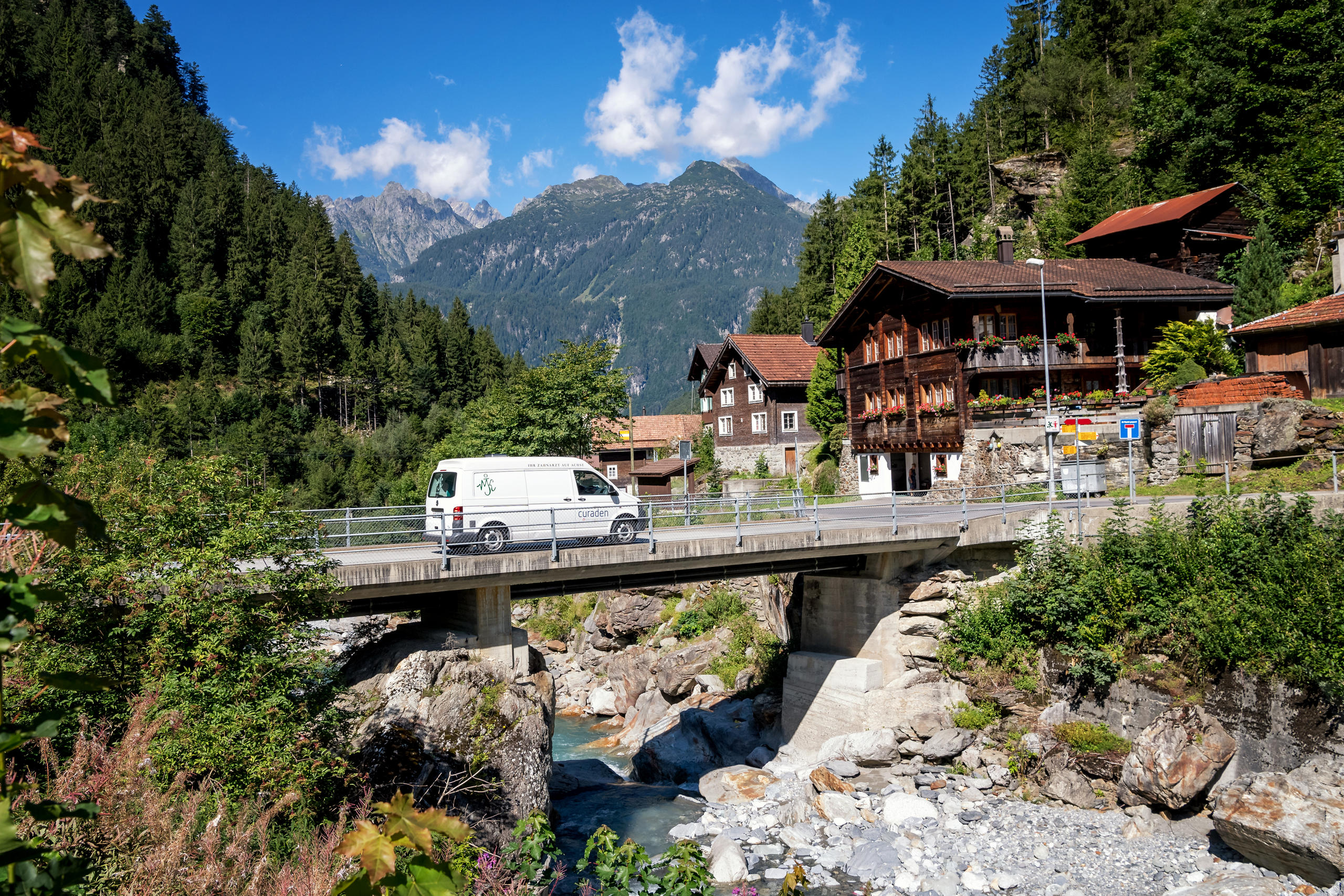Der weisse Bus fährt über eine Brücke in der Berglandschaft