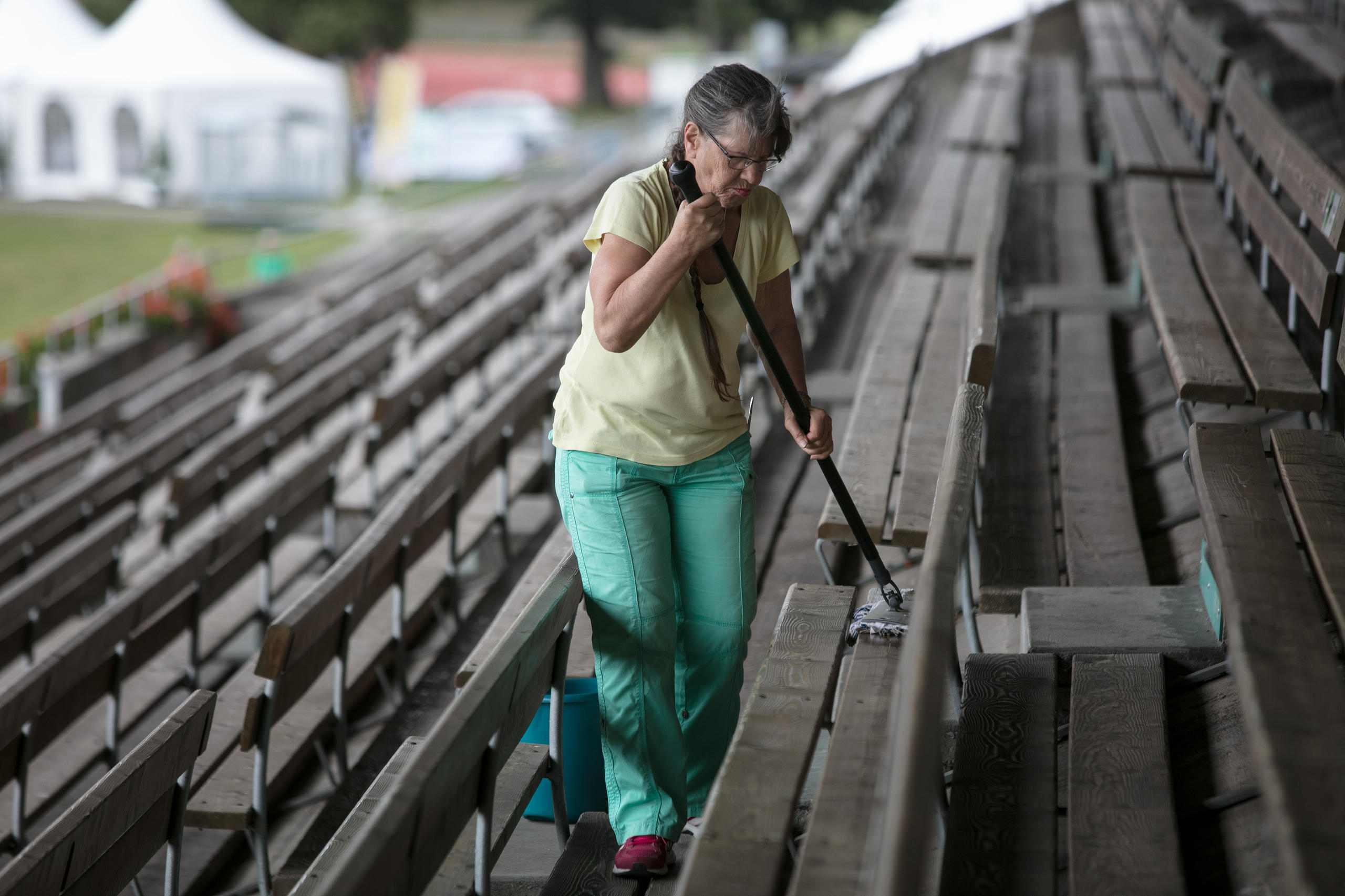 donna pulisce con una scopa una tribuna con panche di legno