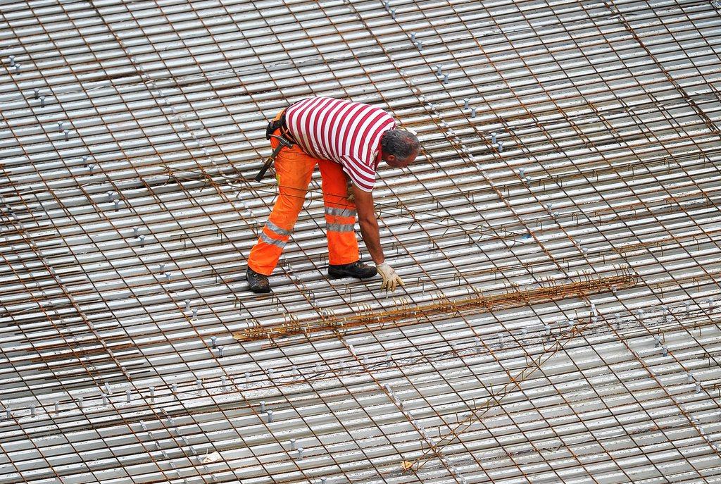 Bauarbeiter auf Flachdach in gestreiftem T-Shirt und orangefarbener Schutzhose