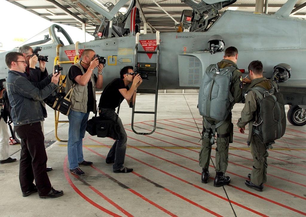 photographers and two other men stand beside an aeroplane