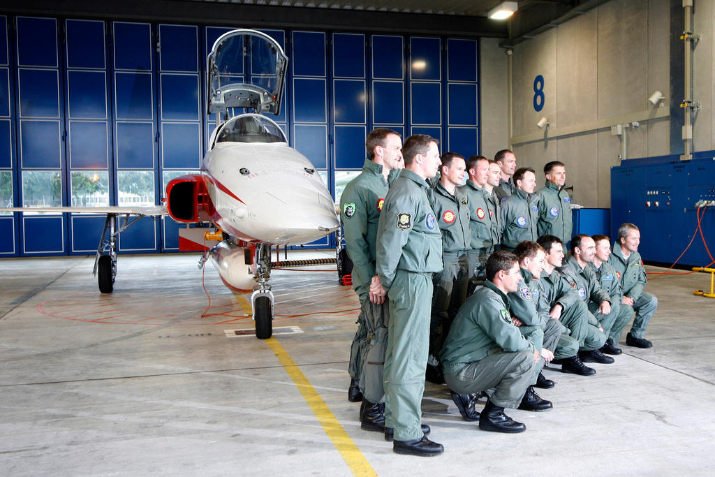 hanger with fighter jet and pilots standing to the right