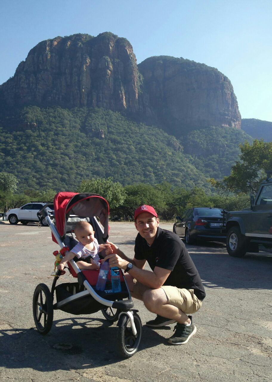 Homme avec un enfant en poussette devant une montagne.
