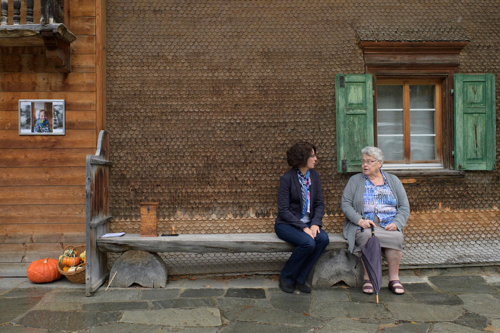 سيدتان تجلسان على مصطبة خشبية أمام إحدى دور البلدية.