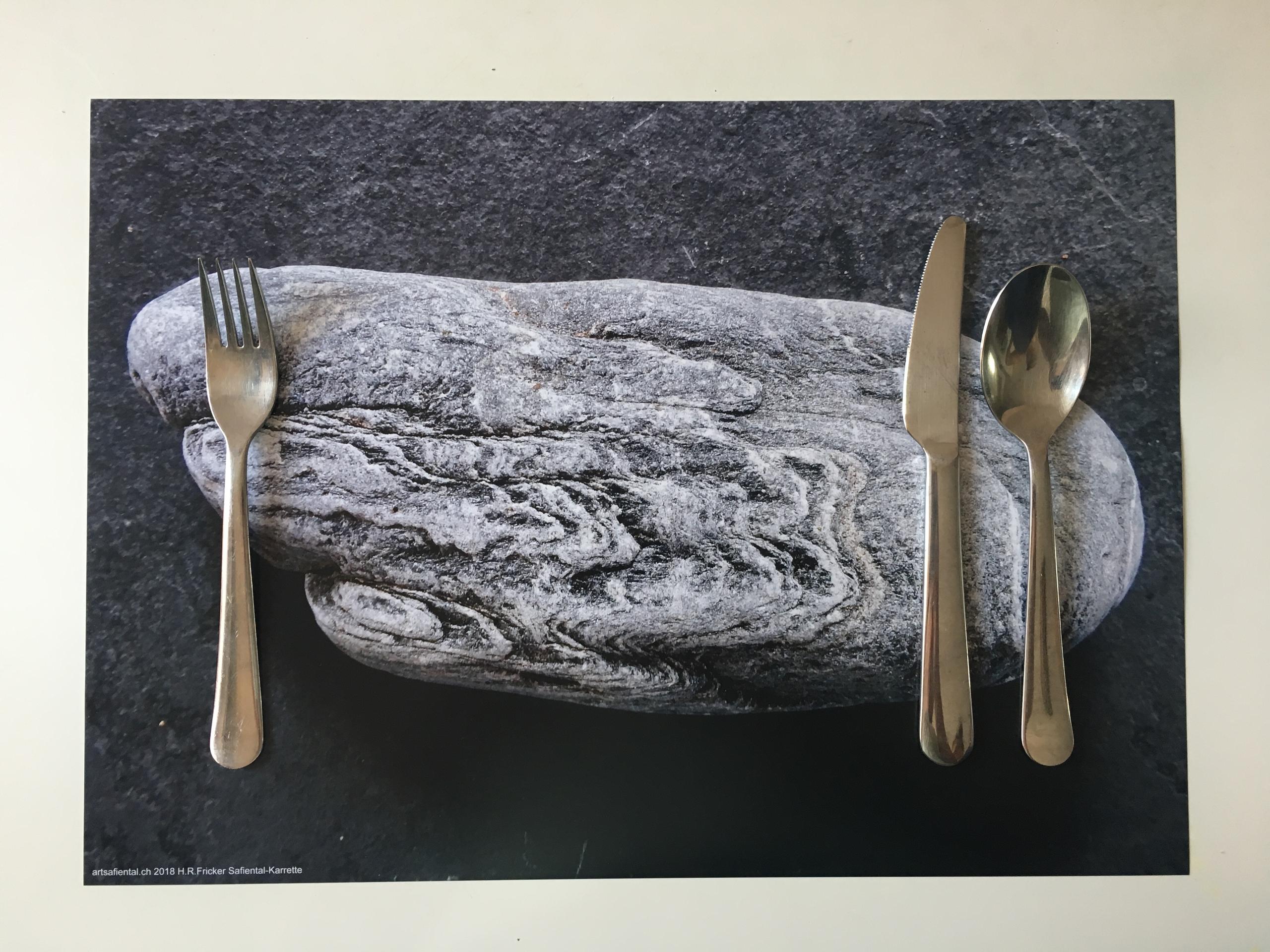 A stone on slate and a knife, fork and spoon.