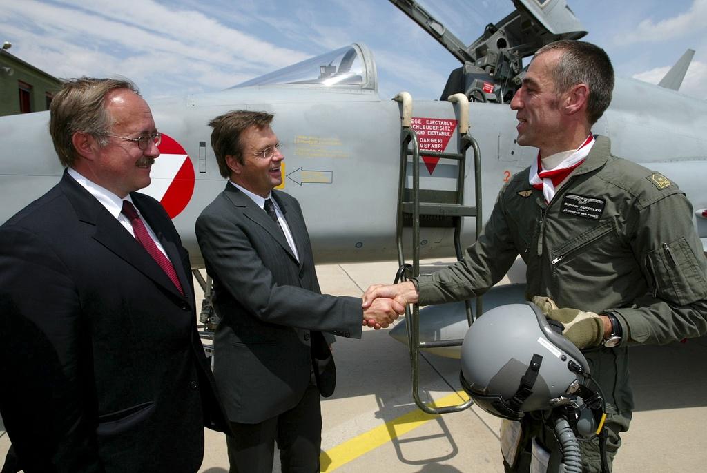 two men shake hands in front of an aeroplane