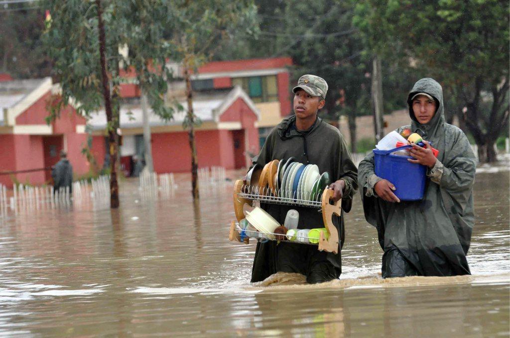 Dos hombres con enseres domésticos avanzan en medio de la inundación.