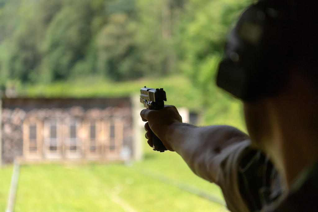 Primo piano di un braccio che punta una pistola verso bersagli, che si vedono sfocati in lontananza