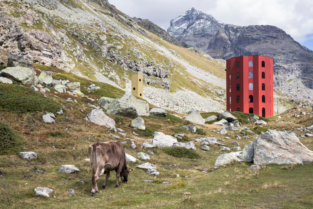 Una vaca pace delante de una obra arquitectónica roja en un paisaje alpino