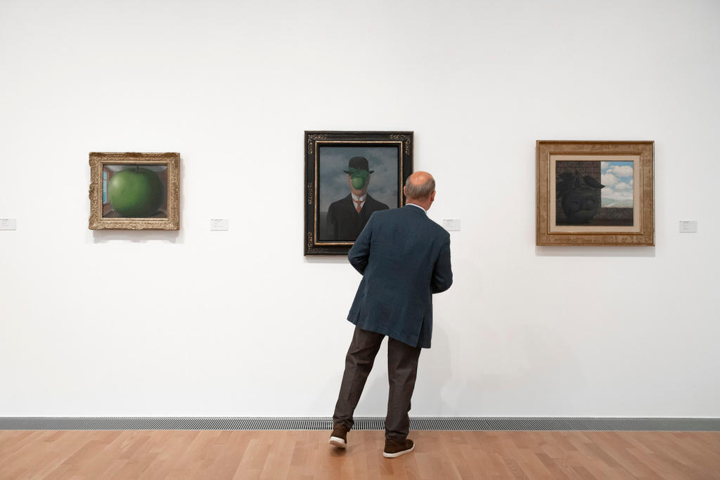 Una sala del museo luganese con tre quadri appesi e un visitatore che osserva uno dei quadri più famosi di Magritte