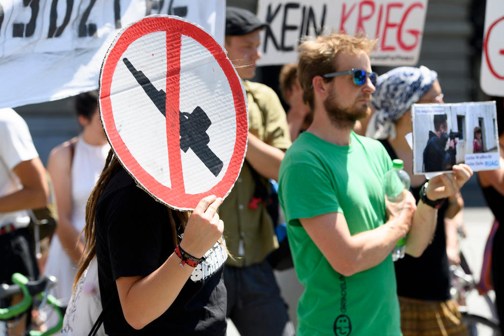 An einer Demonstration hält eine Person einen Karton in der Hand, auf dem ein Maschinengewehr durchgestrichen ist.