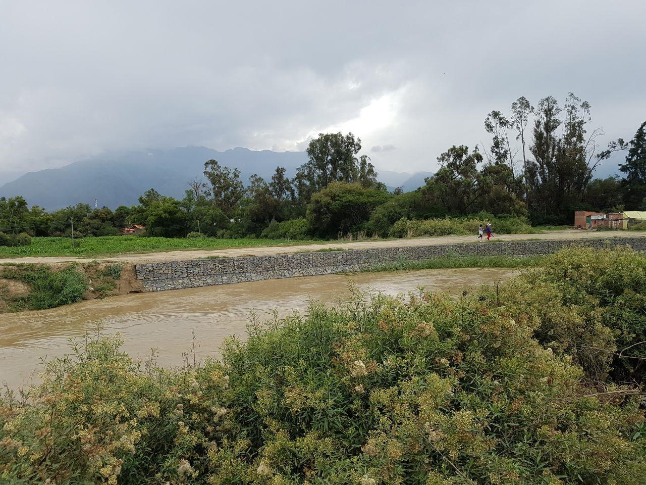 fiume di colore marrone e due persone che camminano sull argine