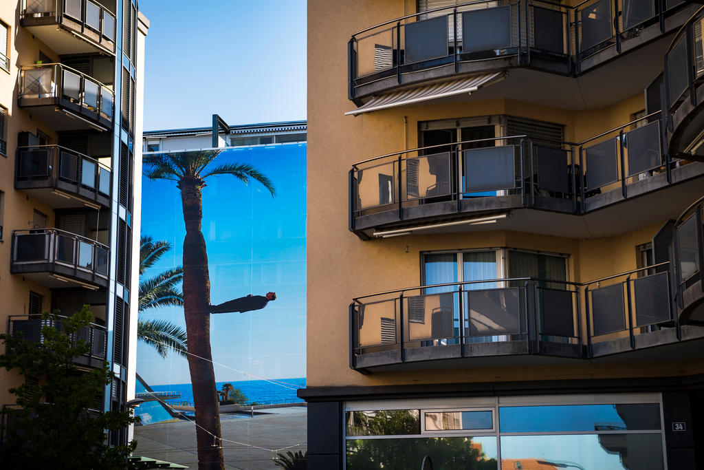 Blick zwischen Häusern hindurch auf eine Fotografie einer Palme am Meer.