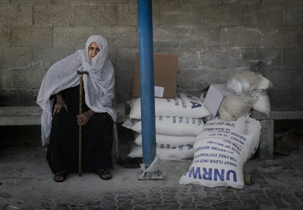 Donna anziana siede di fianco a dei sacchi con aiuti dell Unrwa