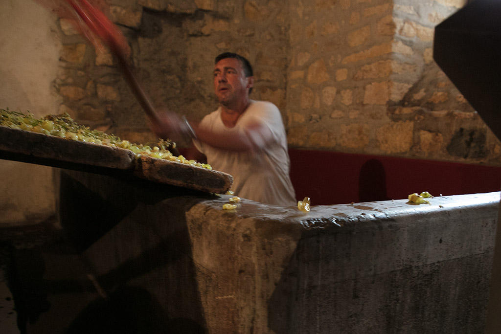 A man shovels grapes from a large maceration tank.