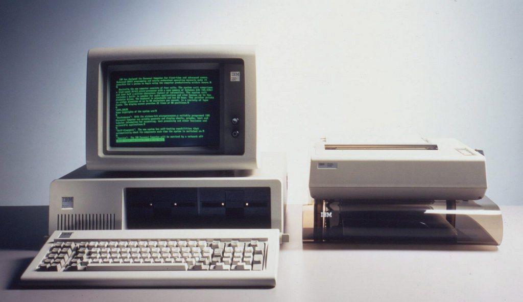 Immagine frontale di un personal computer con vecchio monitor in verde/nero e stampante