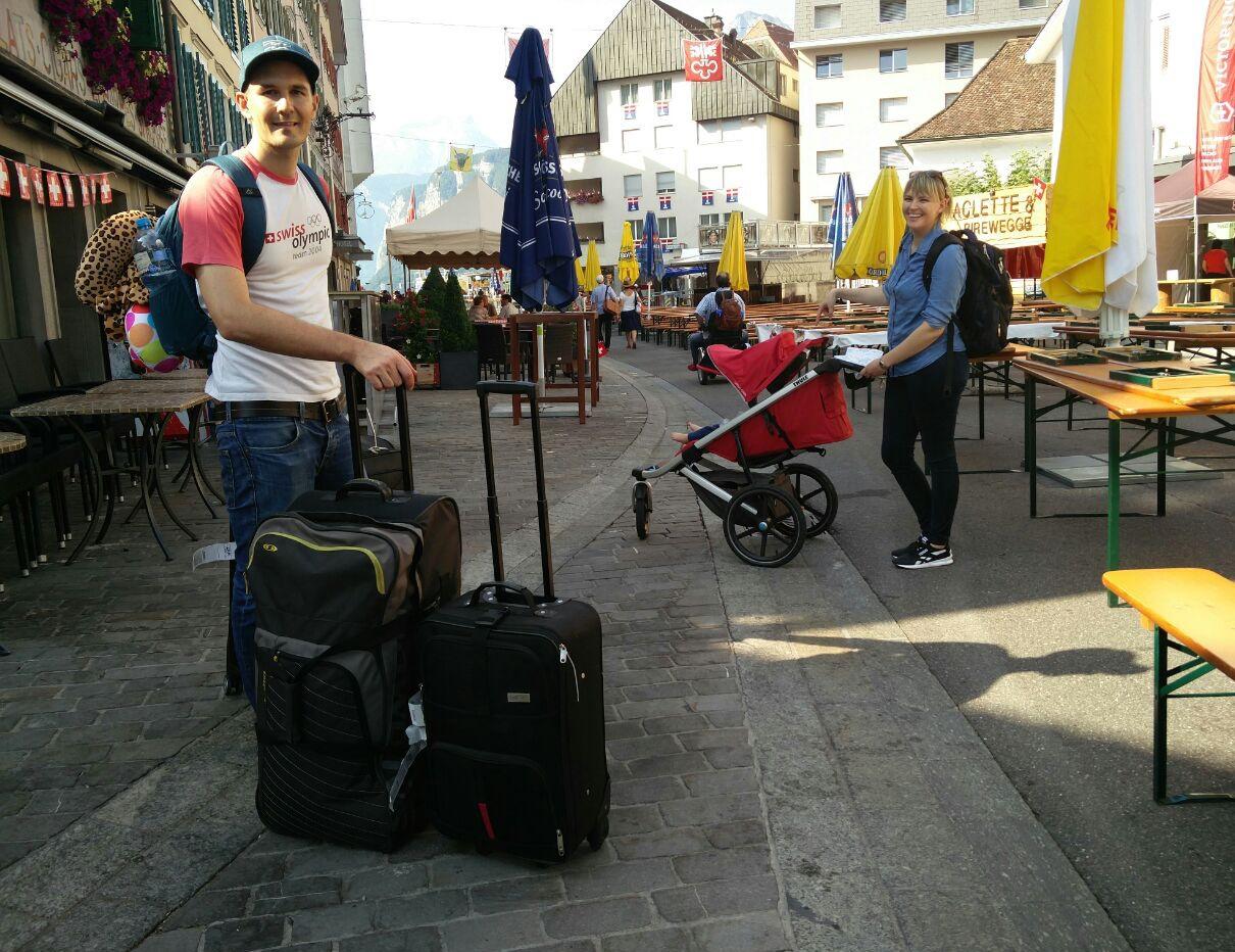 Dos adultos con maletas y un bebé en su carriola en la calle de una ciudad antigua.