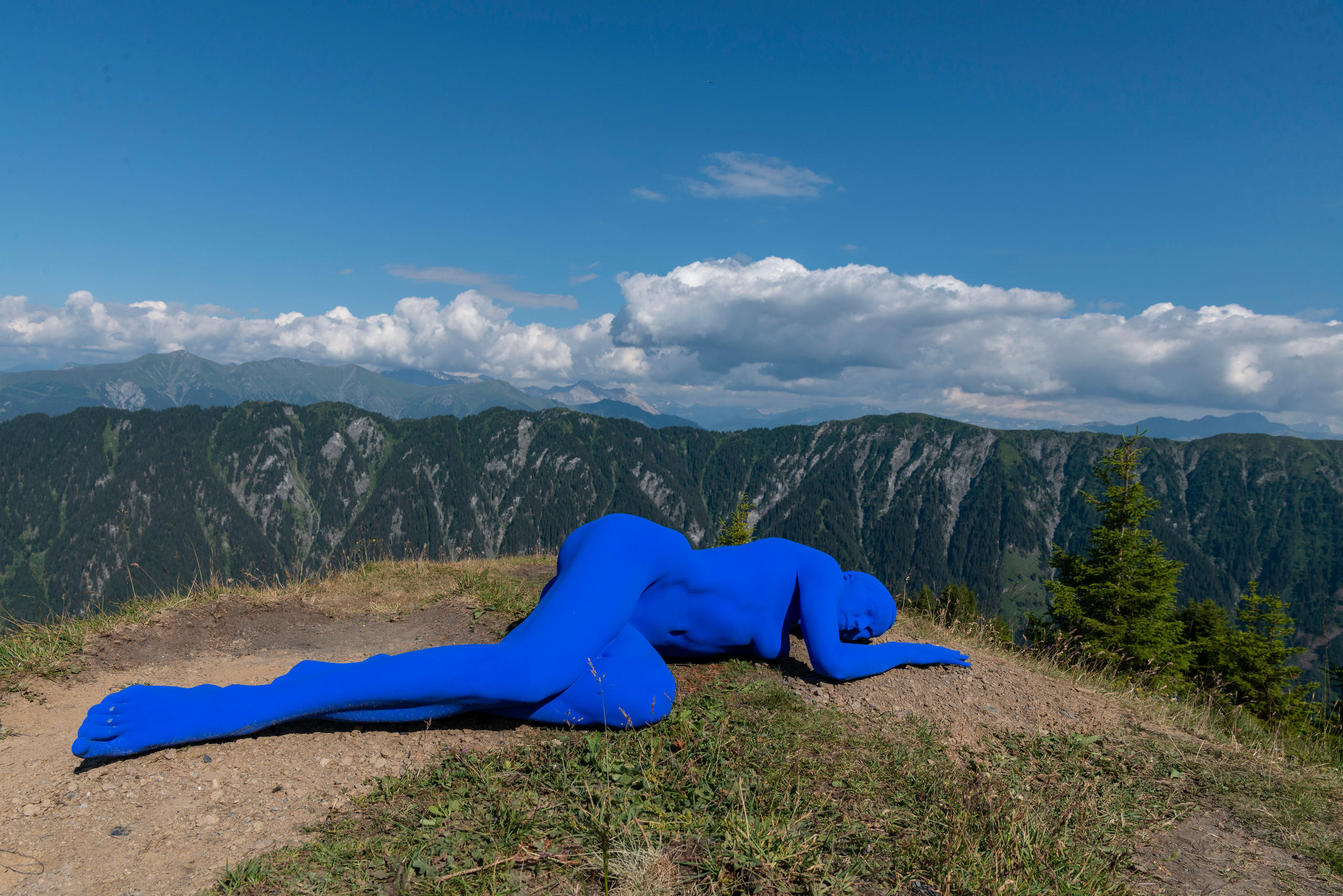 Blue figure lying on their side in the landscape.