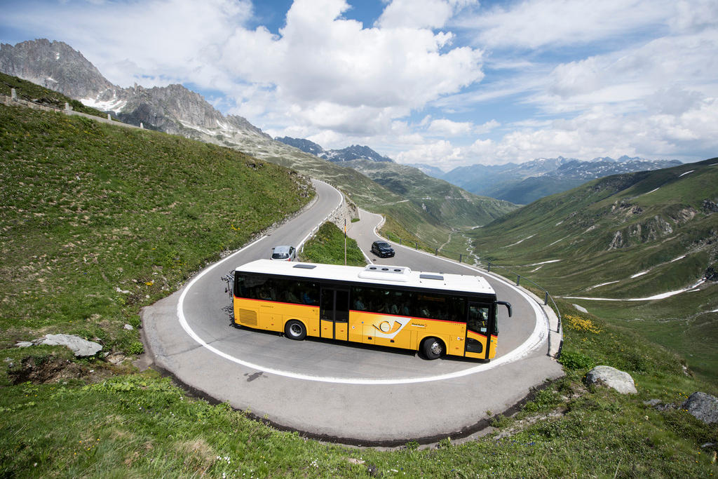 Foto grandangolare di un bus AutoPostale che affronta una curva a gomito su una strada di montagna