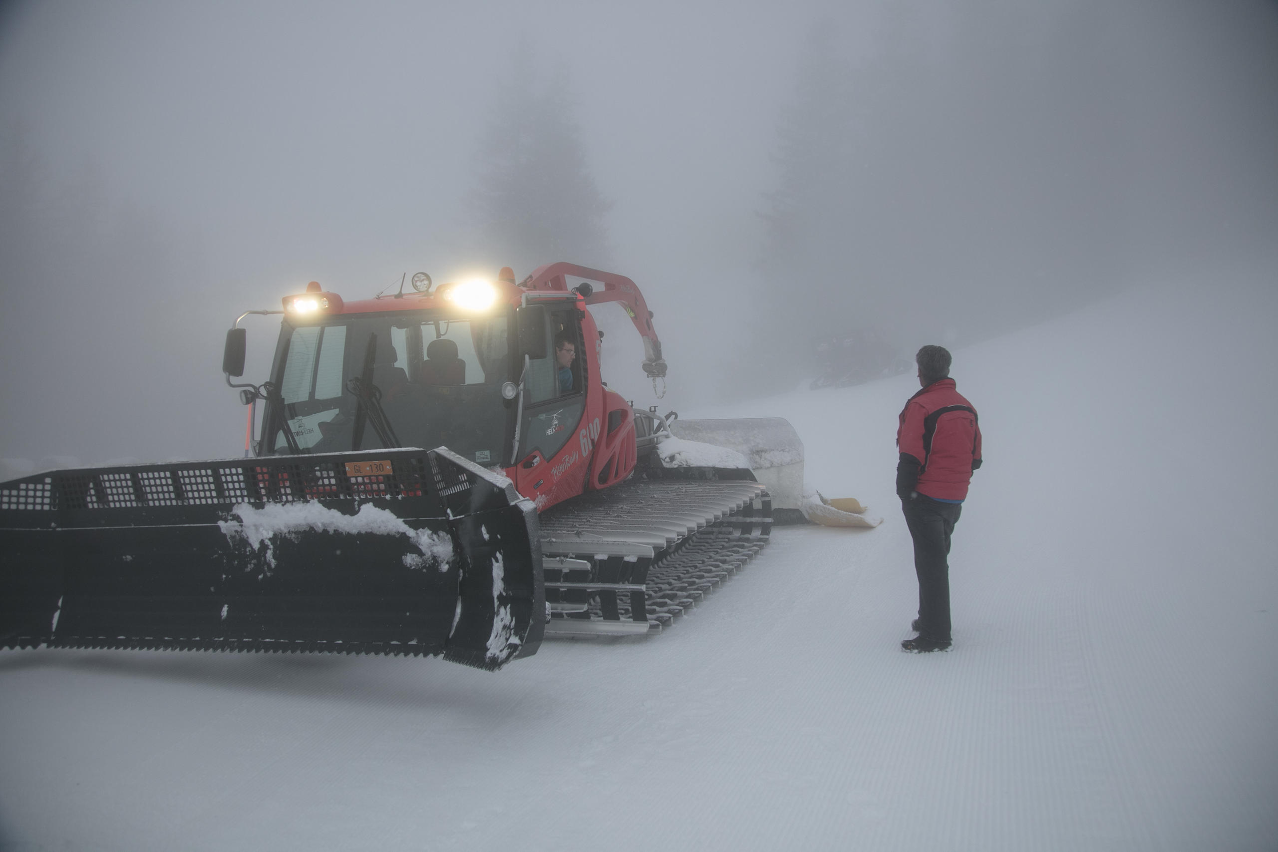 Mitten auf der Piste redet der Pistenbullifahrer mit einem Mann