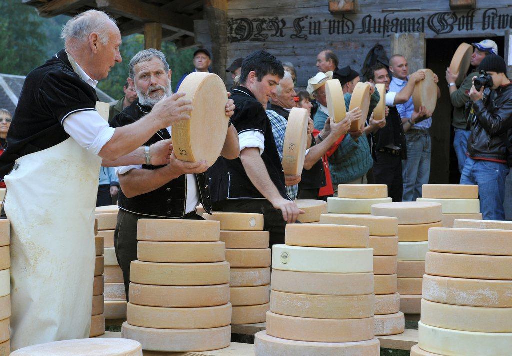 Men pass wheels of cheese taken from piles of wheels