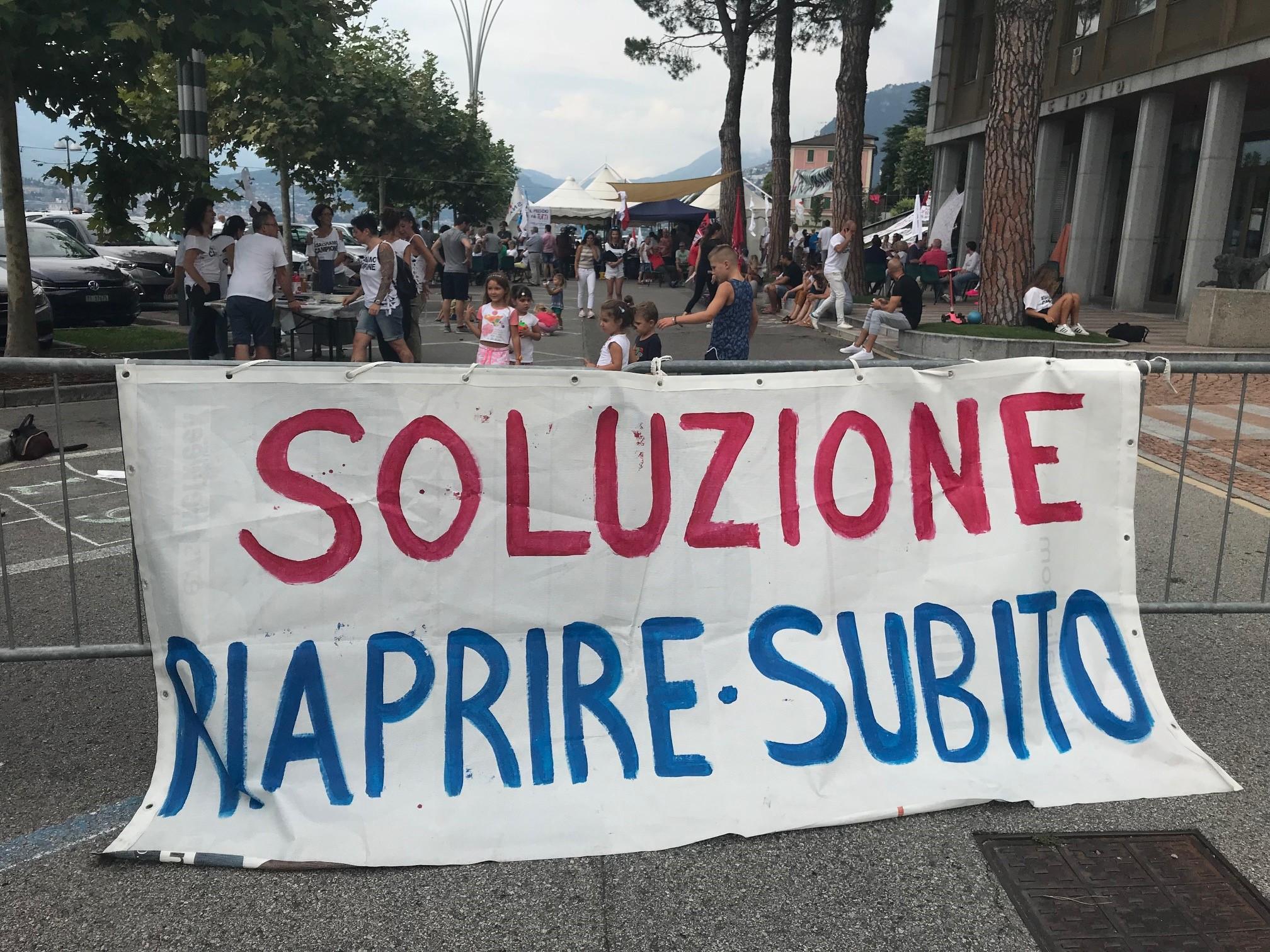 Uno striscione davanti al presidio in piazza a Campione con scritto soluzione, riaprire subito