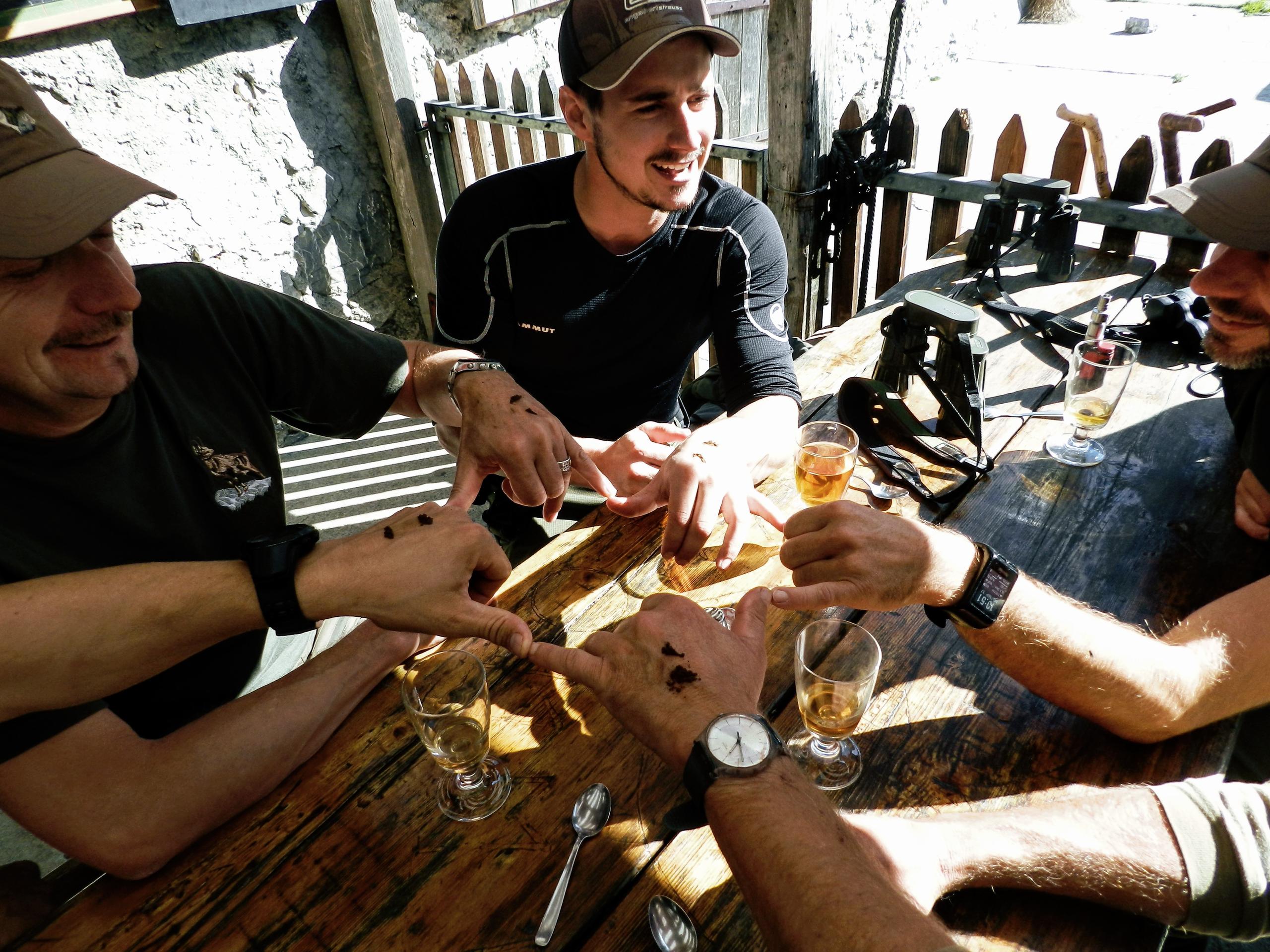 Men at outdoor table prepare a toast with snuff