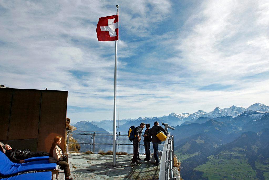 People at the foot of a Swiss flag in the Alps